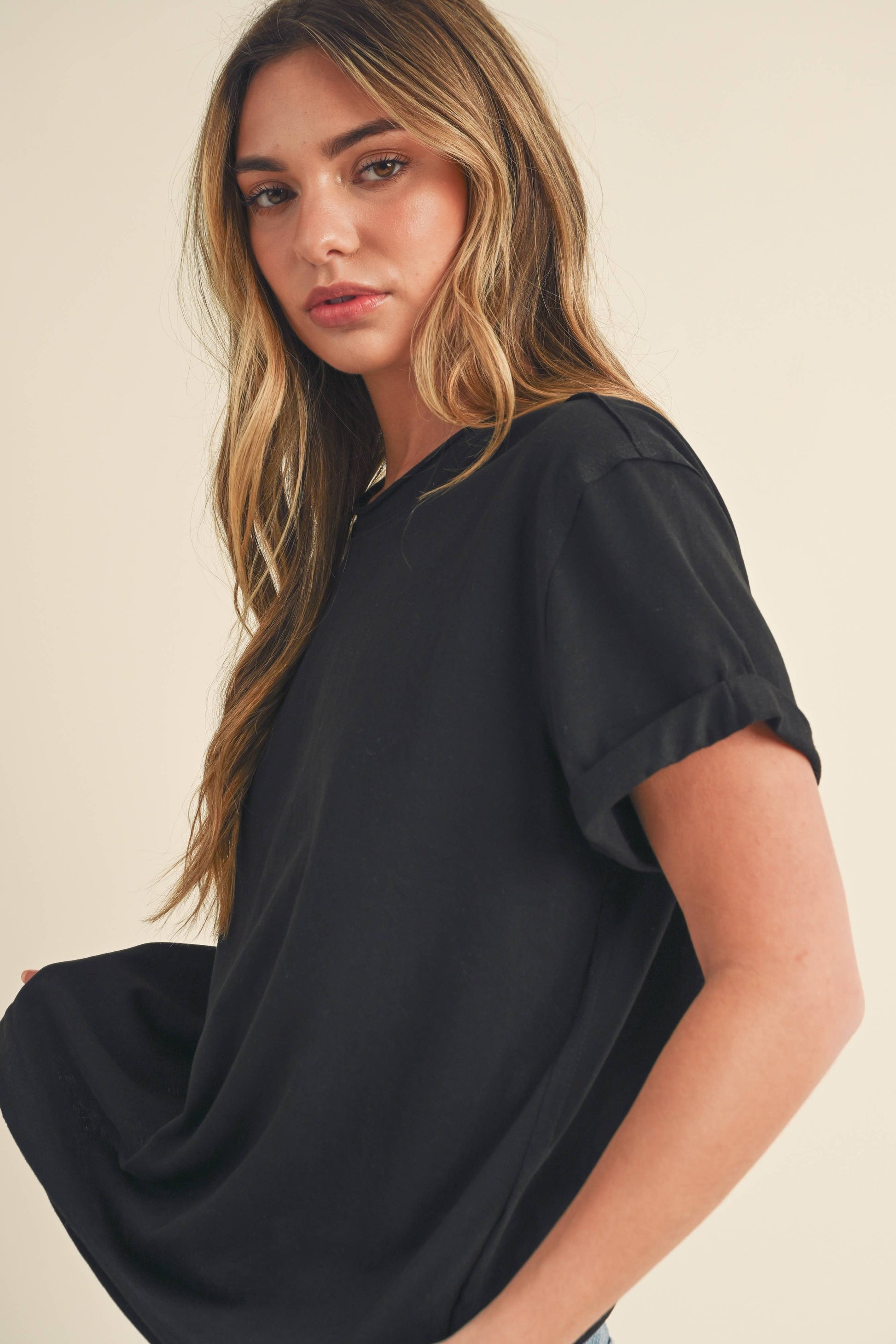 A young woman with long hair looks over her shoulder, wearing a loose black T-shirt. The background is neutral, creating a calm tone.
