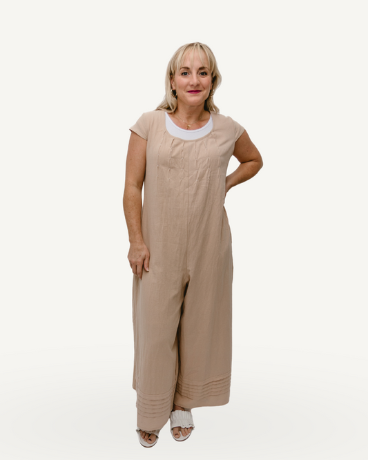 A woman in a beige jumpsuit, with short sleeves, stands confidently.