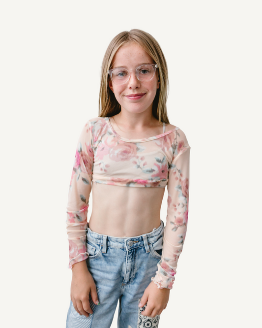 A young girl with glasses wearing a Girlee Long Sleeve Floral Mesh top.
