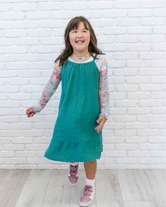 A little girl wearing a Girlee Long Sleeve Floral Mesh dress in green with pink shoes.