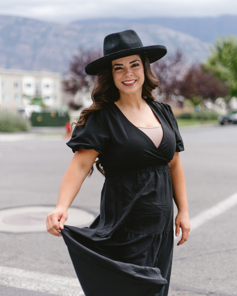 A woman dressed in a black dress and hat walks down the street