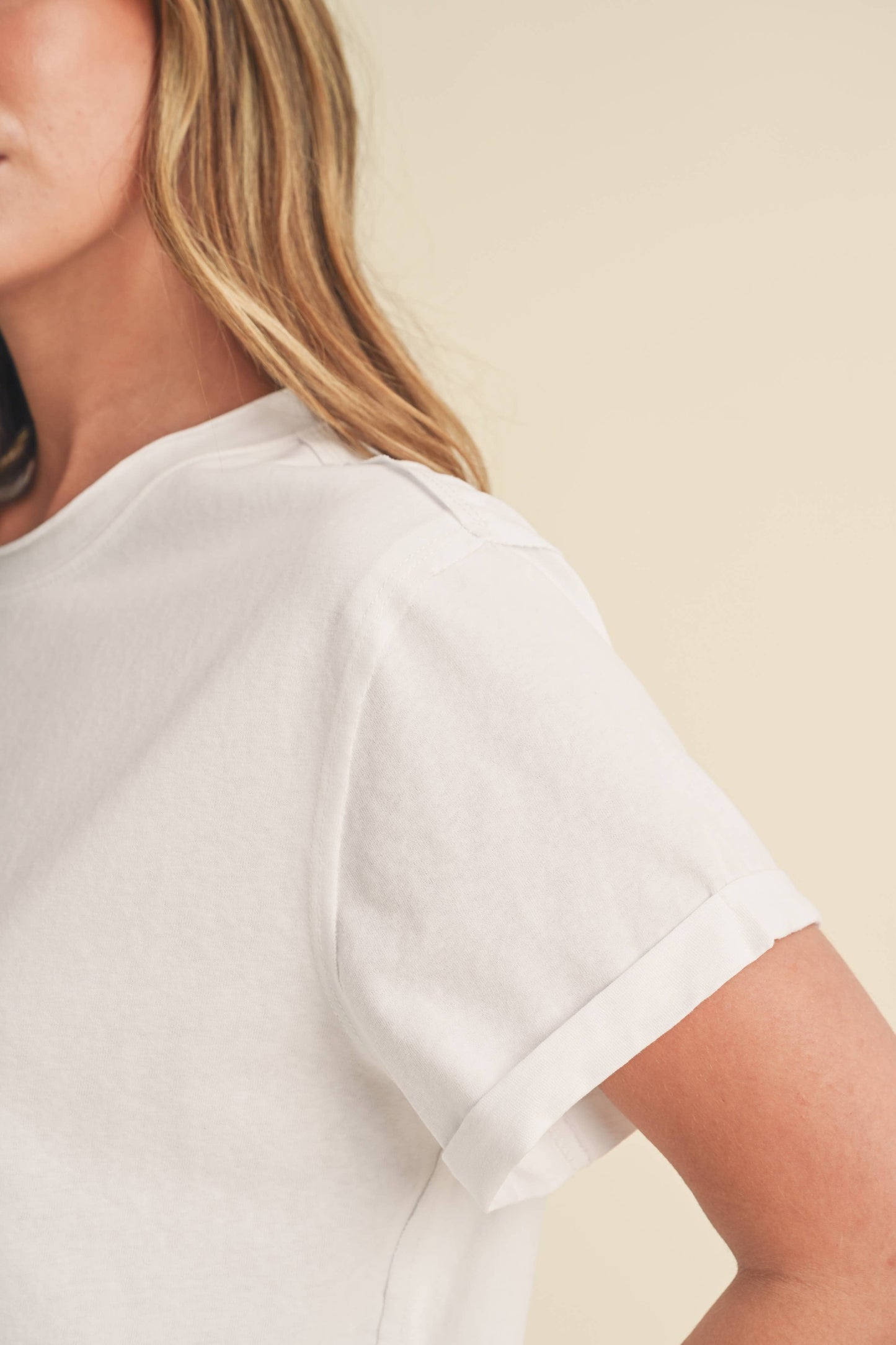 Close-up of a person with long hair wearing a plain white T-shirt against a light beige background. The image conveys a casual and relaxed tone.