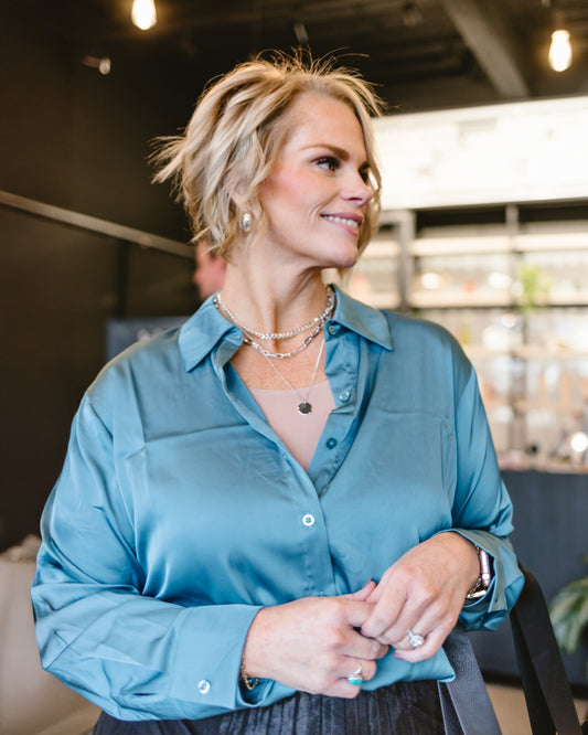 Woman wearing a teal satin shirt layered over a nude Halftee, accessorized with layered necklaces and posing in a modern indoor setting - Halftee