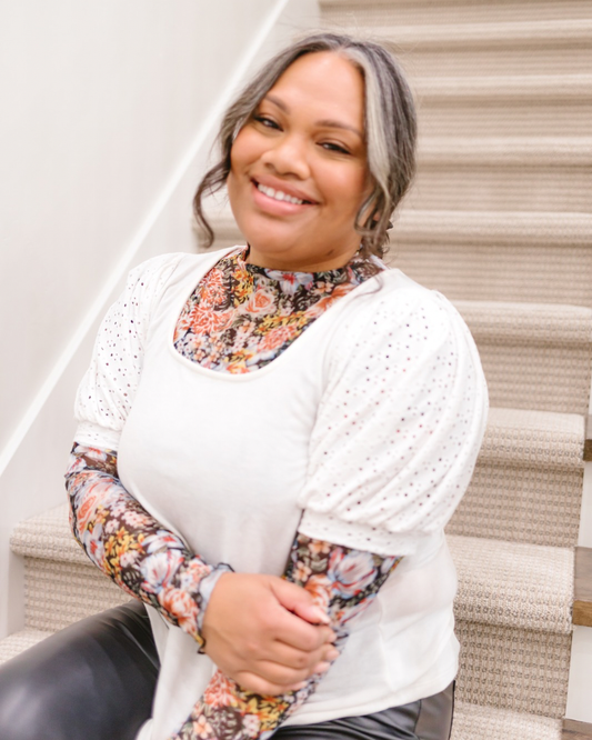 A woman in a white top and floral print pants sits gracefully on the stairs, exuding a relaxed and stylish demeanor.