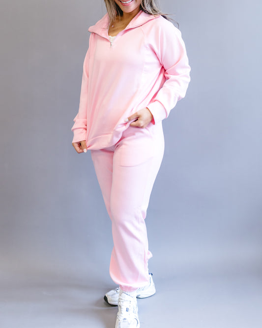 Woman with long highlighted hair modeling a comfortable light pink sweat suit with a silver zipper and white sneakers.