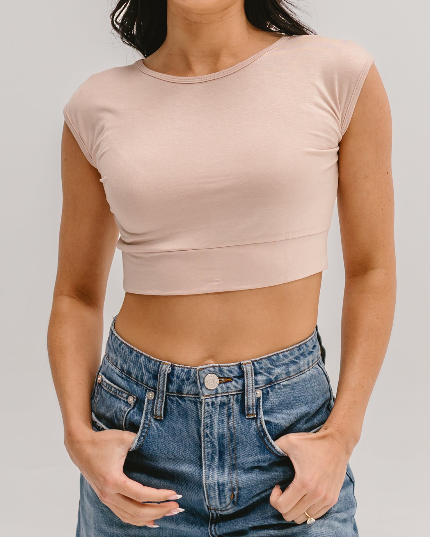 Woman wearing a beige Halftee crop top with short sleeves and blue denim jeans