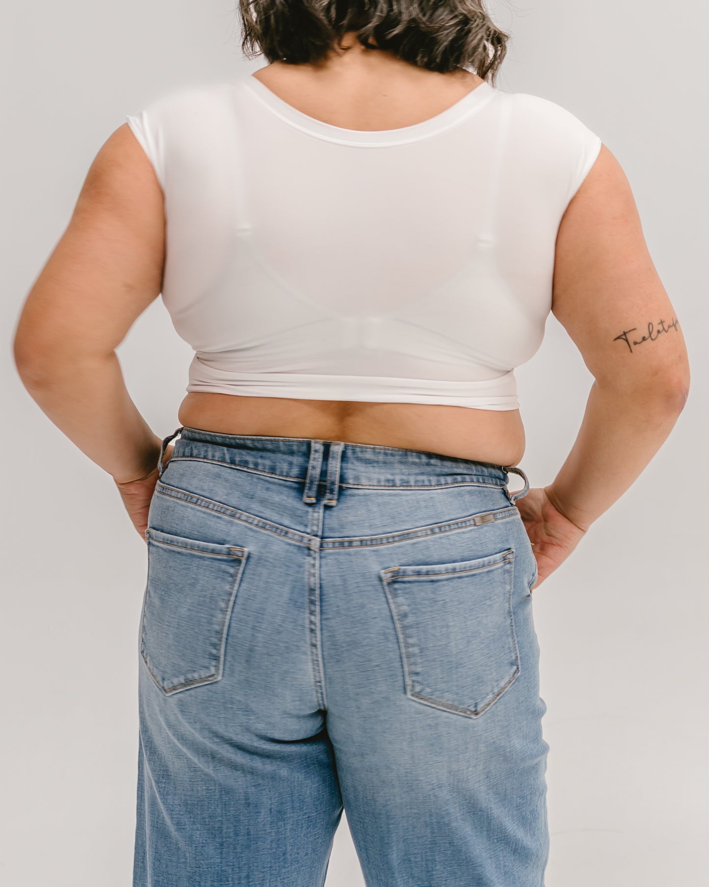 Woman wearing a white Halftee crop top with short sleeves and blue denim jeans, back view