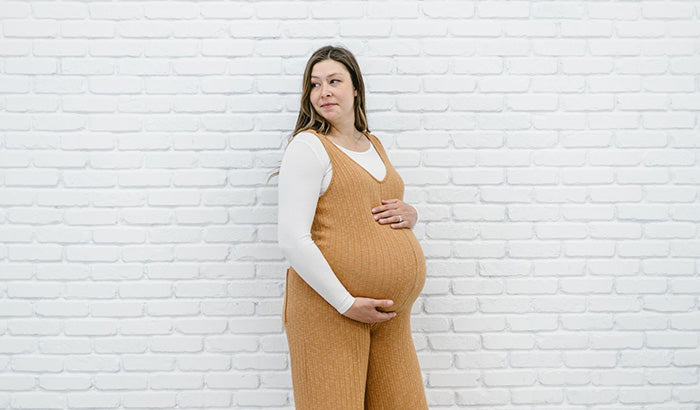 A pregnant woman in a mustard jumpsuit, layering shirts, mid sleeve shirt, with bra alternatives.