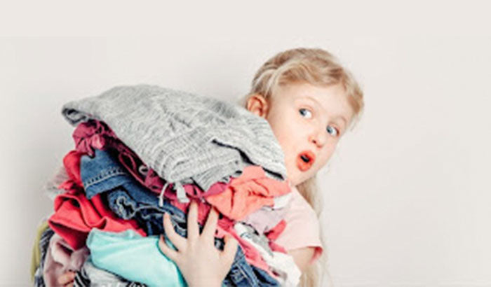 A young girl holding a stack of clothes, showcasing Layering Fashion trend.