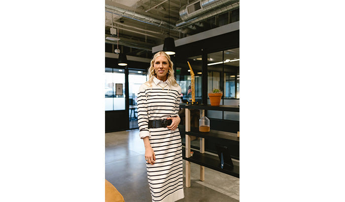 A woman in a striped dress stands confidently in a modern office, showcasing her stylish yet modest wardrobe staples.