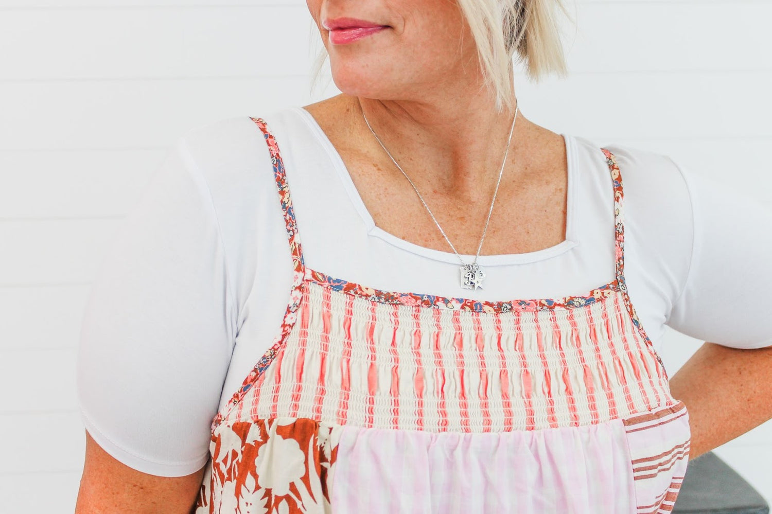 A woman wears a white tee under a patchwork pinafore dress with pink stripes and floral patterns, accessorized with a silver necklace.