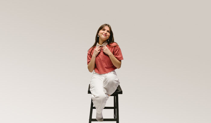 Woman sitting on chair, hands on chest, wearing modesty shirts, shirred maxi dress, flared sleeve dress.