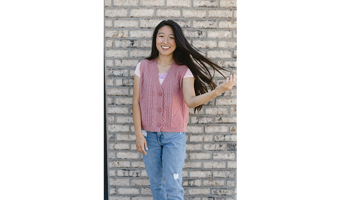 A young woman wearing jeans and a pink sweater, showcasing fashionable shirts, layered shirts, and dress tees.