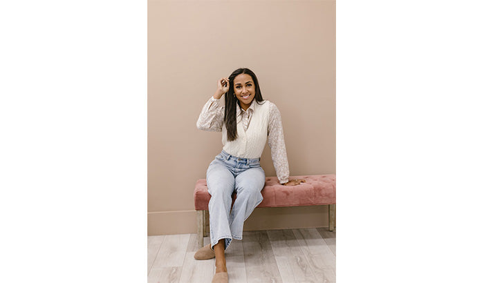 Woman in jeans and vest sitting on pink bench, wearing crew neck tank top with mesh and bell sleeves