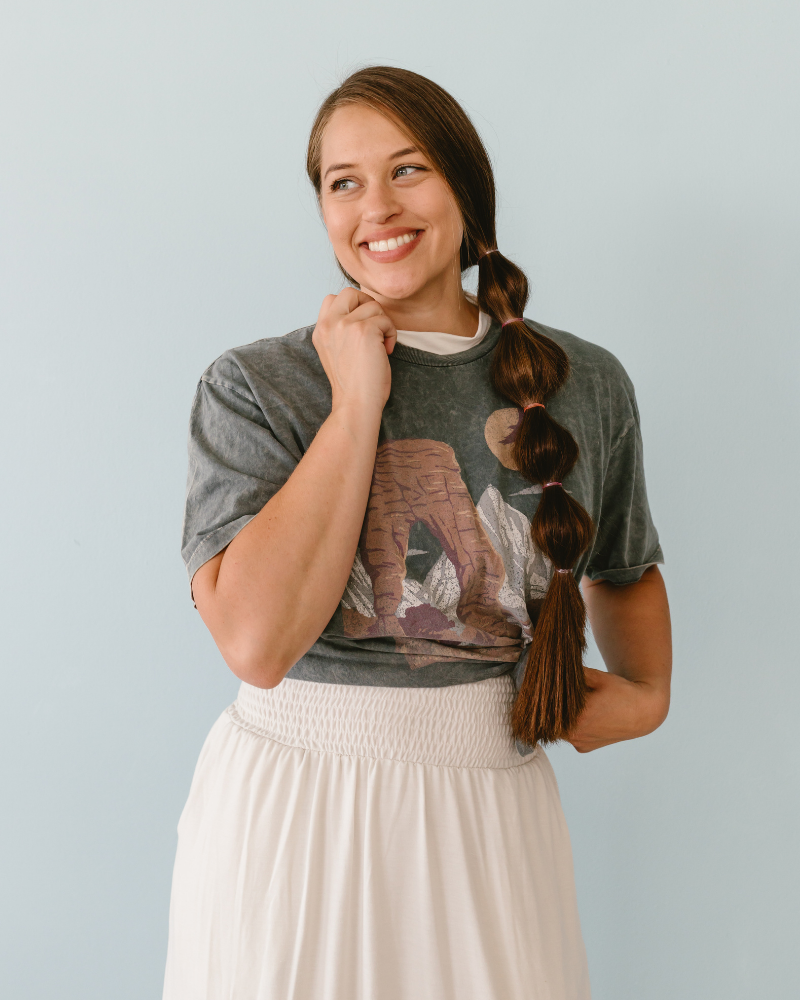 A woman wearing a white skirt and a t-shirt with a cat on it. She is also wearing a mock neck sleeveless front.