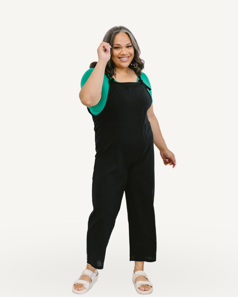 A woman wearing a loose black overall jumpsuit with a green top.