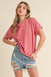 Young woman in a pink T-shirt and distressed denim shorts poses confidently against a beige backdrop, conveying a casual, relaxed mood.