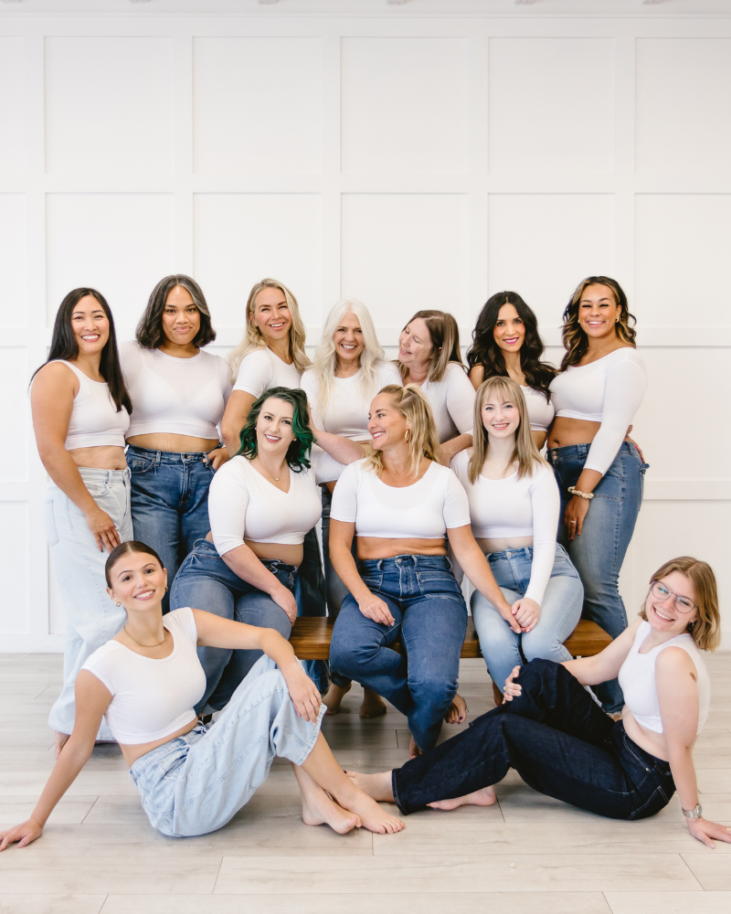 A diverse group of women in fresh white shirts and jeans posing for a photo.