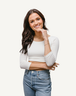 A woman wearing jeans and a white crop top with elbow sleeves and a V-neck.