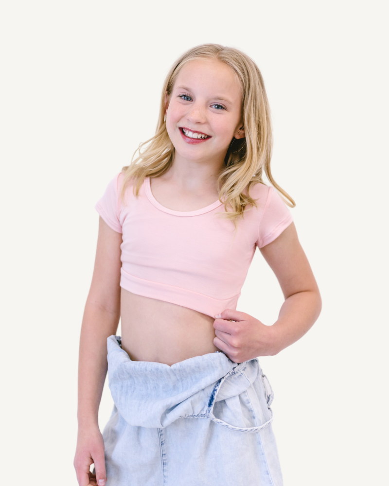 A young girl in a pink shirt and jeans, standing next to a sign that reads 'GIRLEE Boyfriend'.