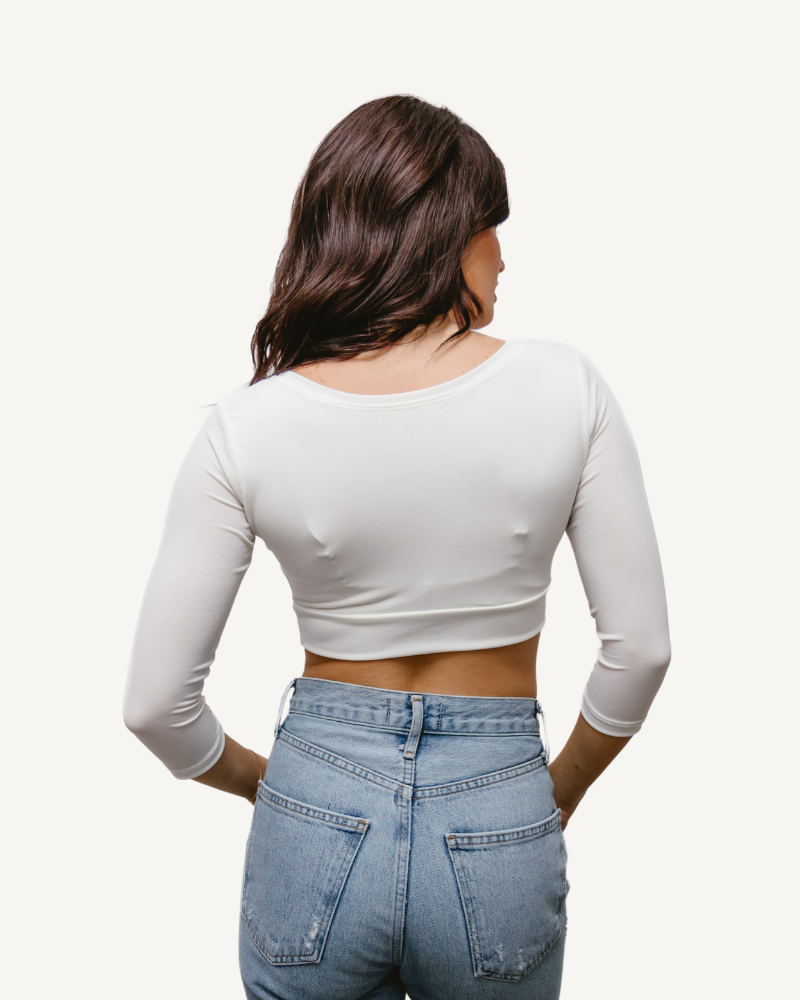 A woman wearing jeans and a white crop top with elbow sleeves and a V-neck.