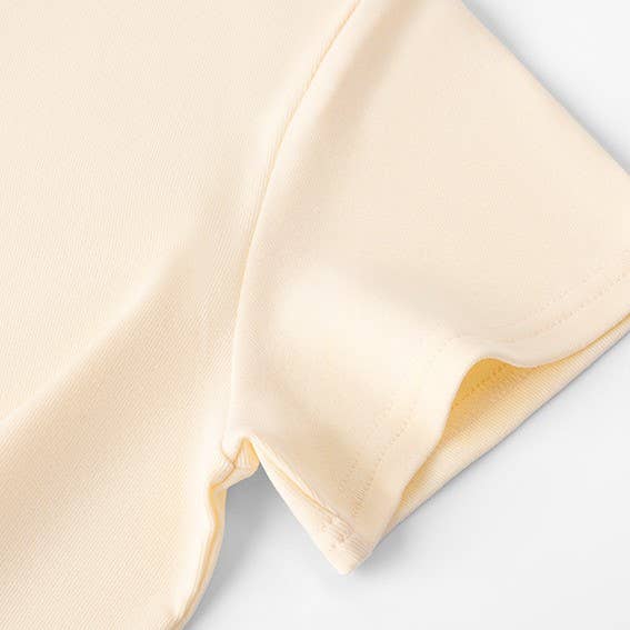 Close-up of a light yellow short-sleeve shirt, showing detailed stitching on soft fabric, evoking a sense of simplicity and comfort.