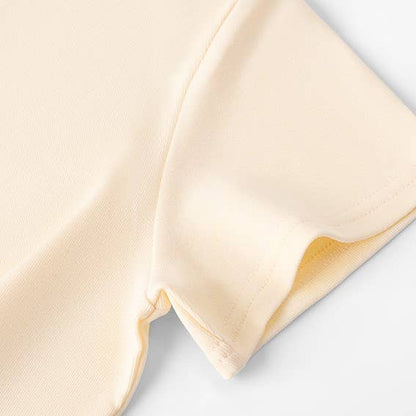 Close-up of a light yellow short-sleeve shirt, showing detailed stitching on soft fabric, evoking a sense of simplicity and comfort.