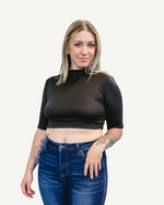 A woman in a black crop top and jeans stands confidently