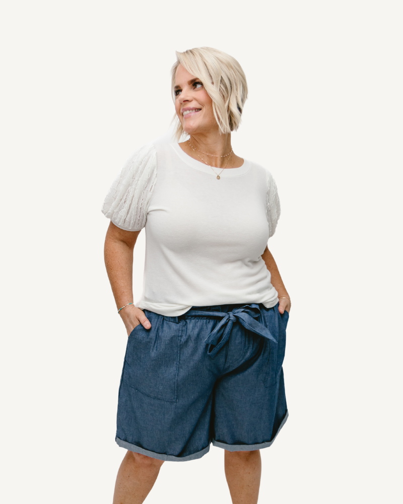 A woman wearing a white shirt and blue denim shorts, showcasing Denim Look Paper Bag Shorts.