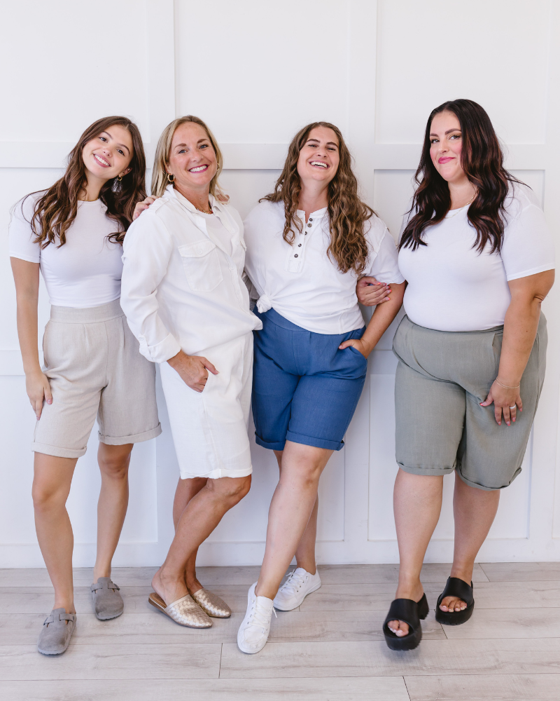 Four women in white shirts and linen shorts posing for a picture.