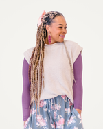 A woman with braided hair wears a purple sweater paired with floral pants, exuding a fashionable and colorful appearance.