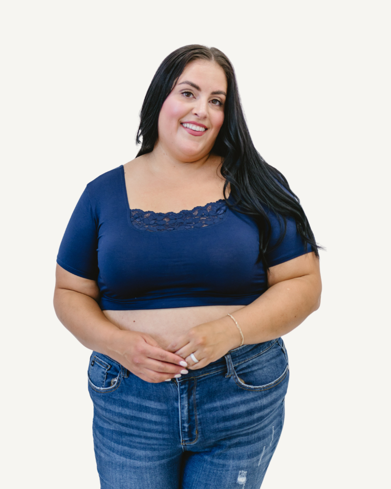 A curvy woman in a navy crop top and jeans, wearing a Peekaboo Short Sleeve Halftee with lace inset.