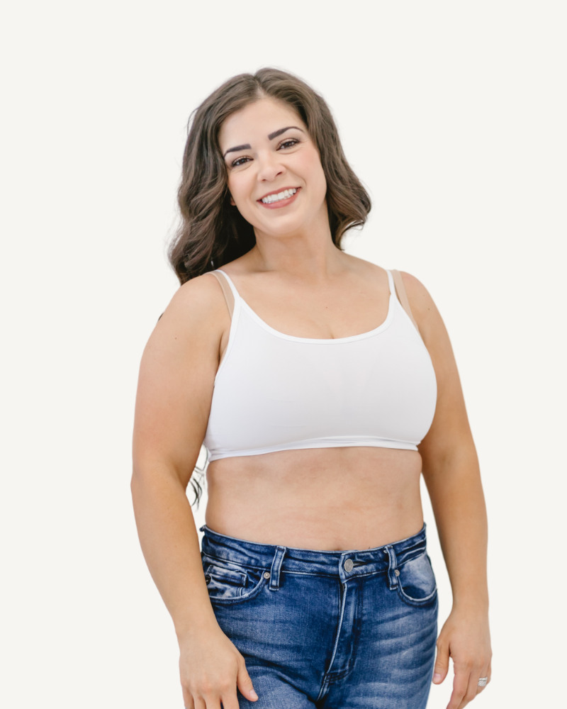 A young woman wearing a white bra top and jeans, standing confidently with a casual pose.