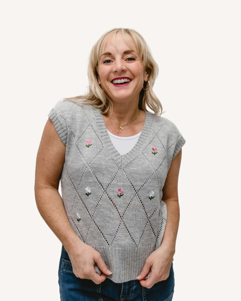 A woman wearing a gray sweater with pink floral details.