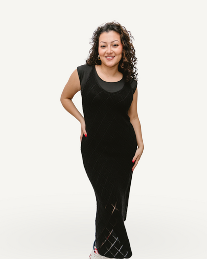 A woman in a black crochet knit dress posing elegantly for the camera.