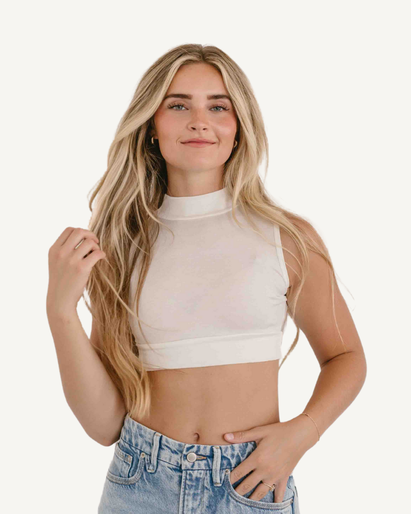 A model wearing a mock neck sleeveless front crop top and jeans, showcasing a trendy and stylish outfit.