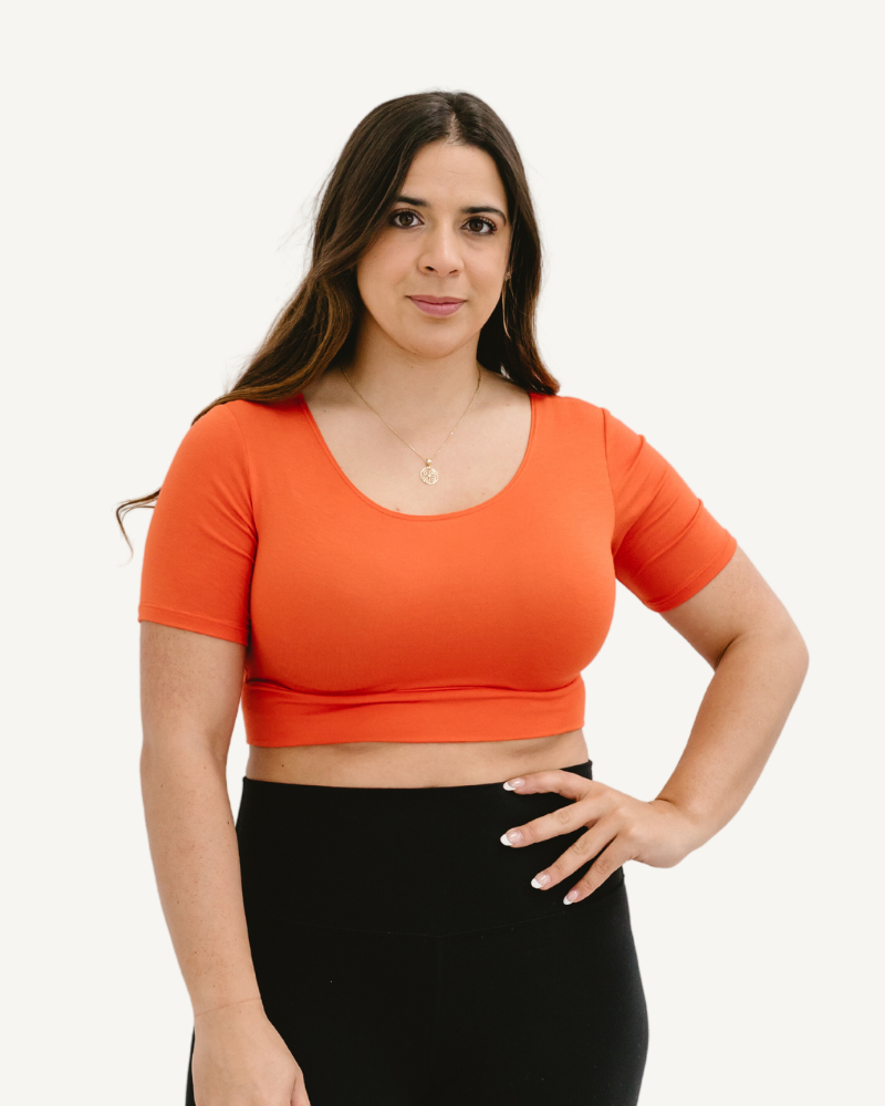 A woman wearing a bright orange crop top and blue jeans, showcasing a trendy and vibrant style.