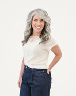 A woman with gray hair dressed in jeans and a white top