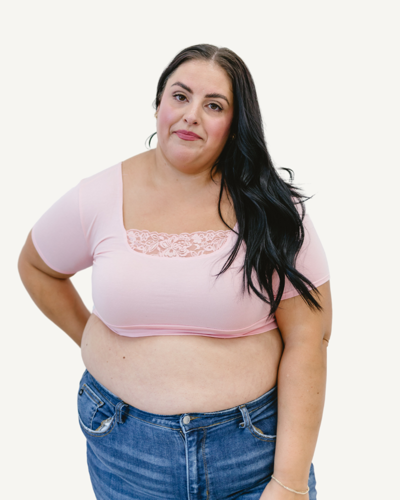 A curvy woman in a pink crop top and jeans, wearing a Peekaboo Short Sleeve Halftee with lace inset.