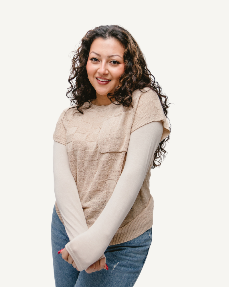 A woman with curly hair wearing a tan top and a Pocket Sweater Vest.