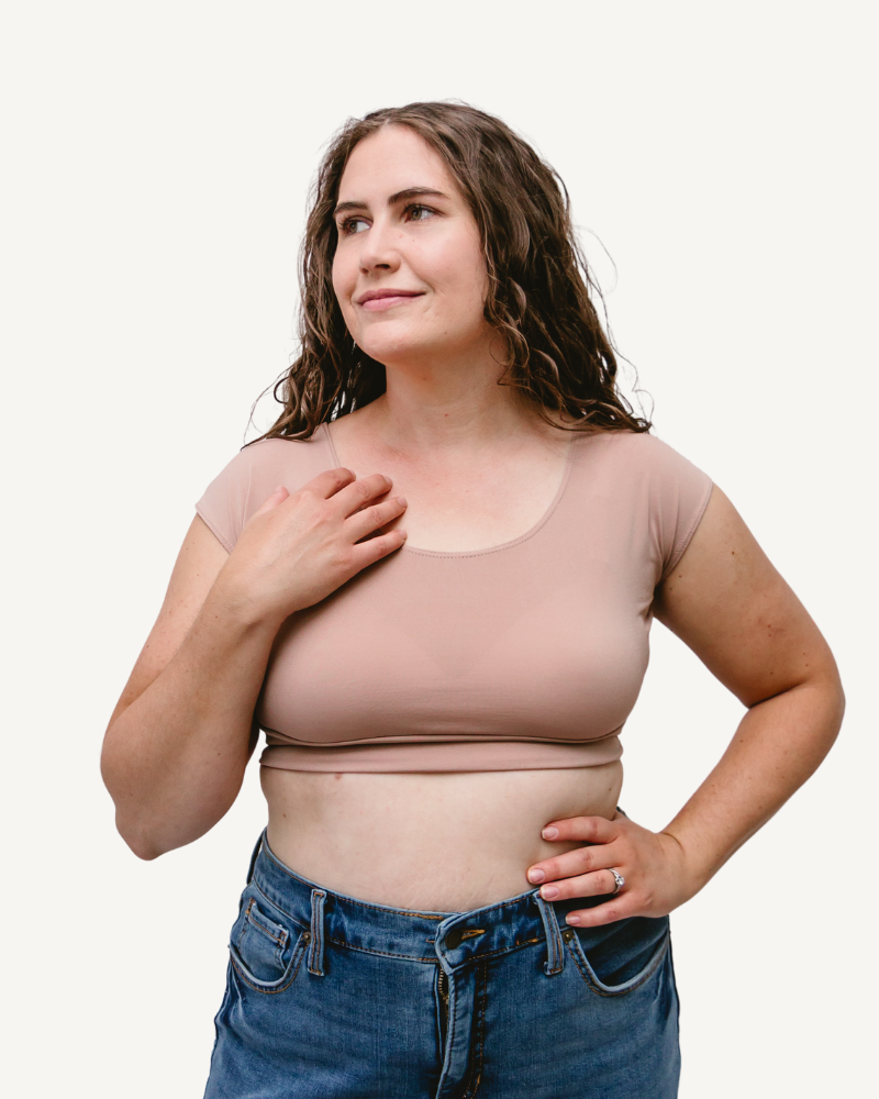 A woman wearing a tan top and jeans, standing confidently with a smile.