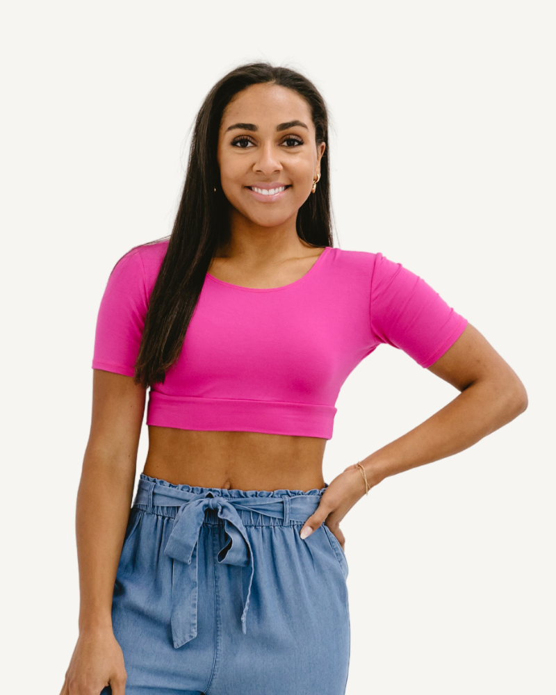 A woman wearing a bright pink crop top and blue jeans, showcasing a trendy and vibrant style.