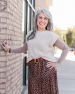 A woman wearing a leopard print skirt and sweater stands confidently, showcasing her stylish outfit and bold fashion choice.