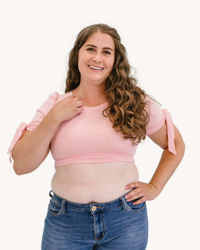 A plus size woman in a pink top and jeans, wearing a Puff Sleeve Halftee with Tie Detail.