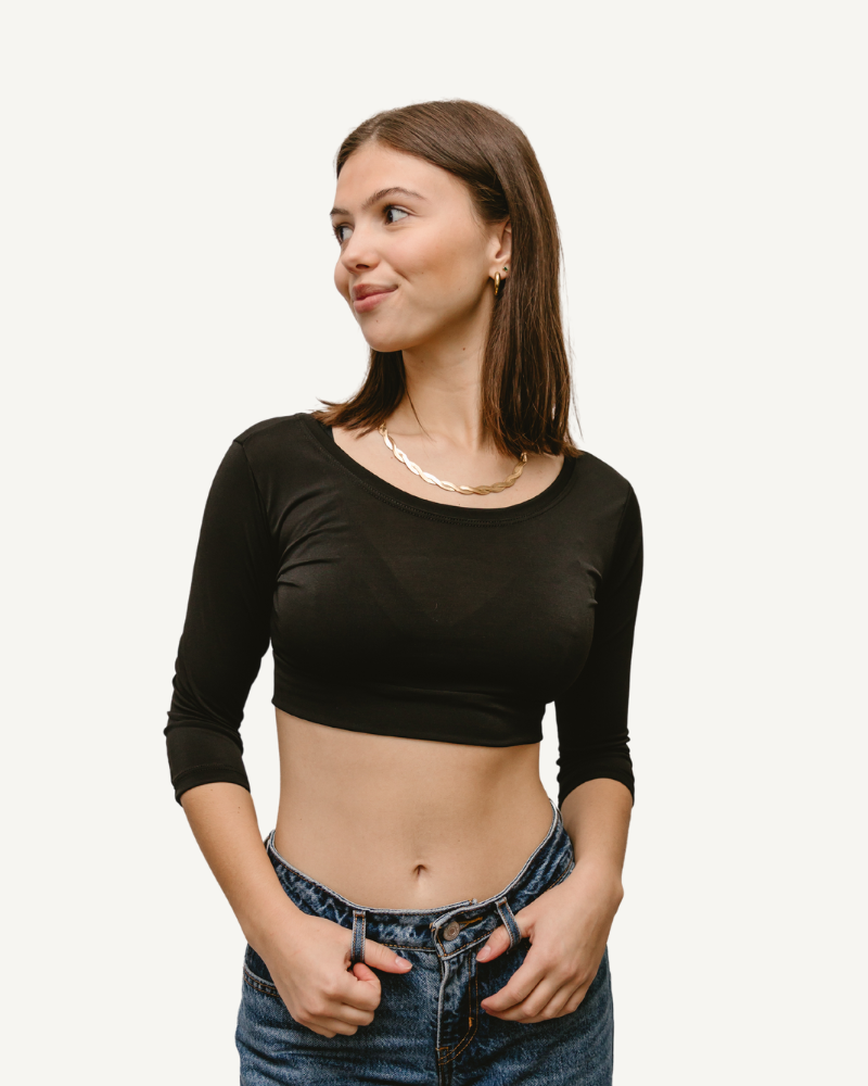 A woman wearing jeans and a black crop top with elbow sleeves and a V-neck.
