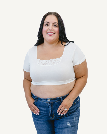 A curvy woman in a white crop top and jeans, wearing a Peekaboo Short Sleeve Halftee with lace inset.