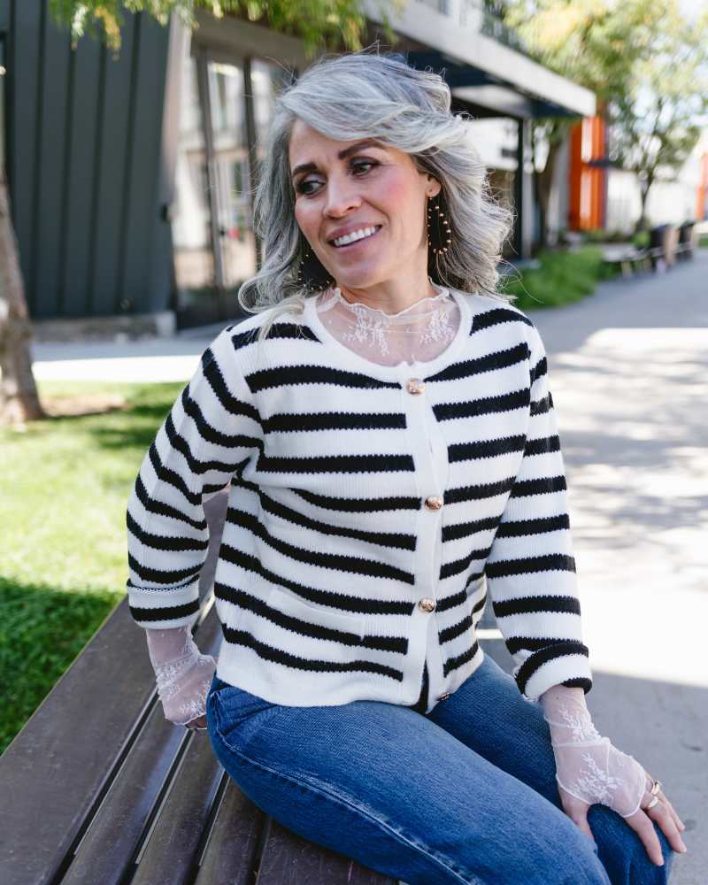 A woman with gray hair wearing a striped sweater sits thoughtfully on a bench