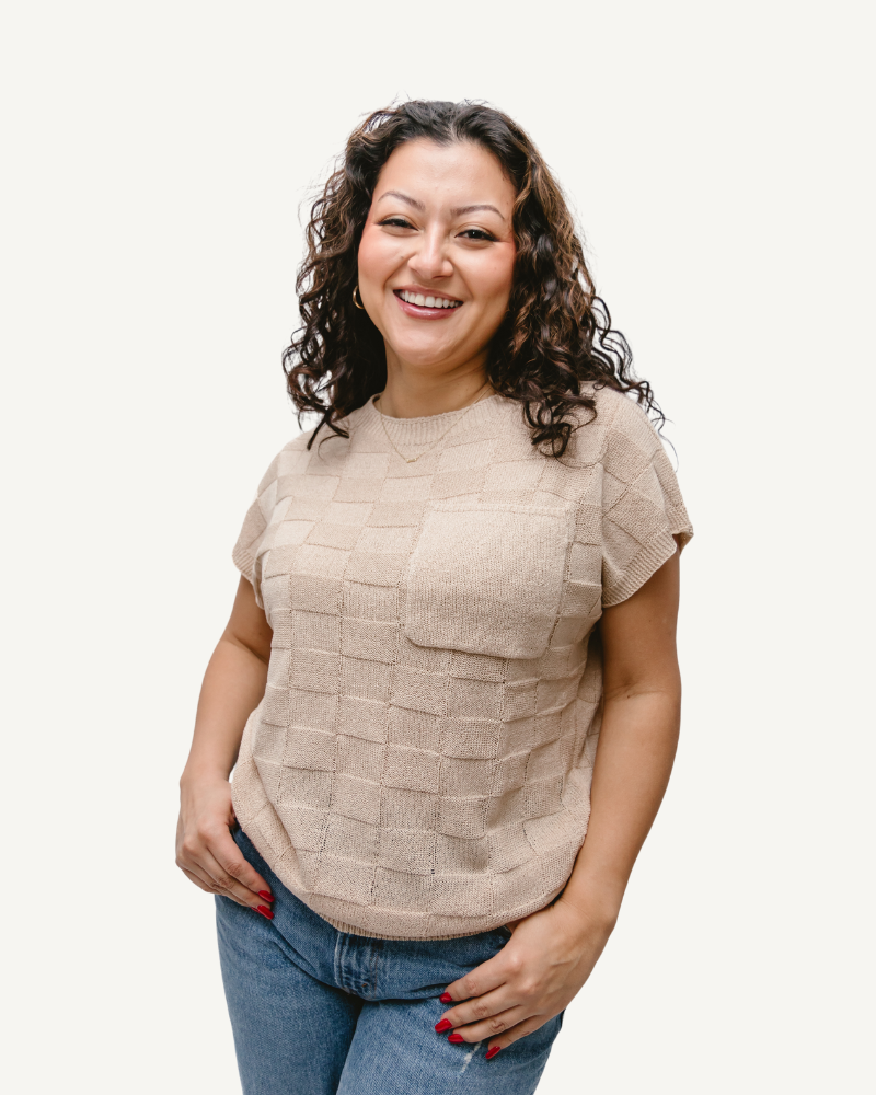 A woman with curly hair wearing a tan top and a Pocket Sweater Vest.