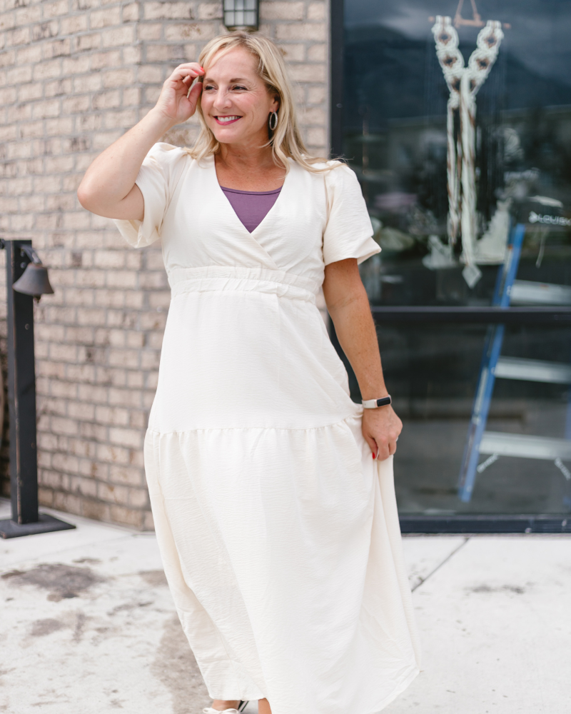 A woman elegantly dressed in a white dress and a purple top.