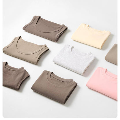 Folded t-shirts in beige, cream, gray, and pink are neatly arranged in rows on a white surface, conveying a sense of order and simplicity.